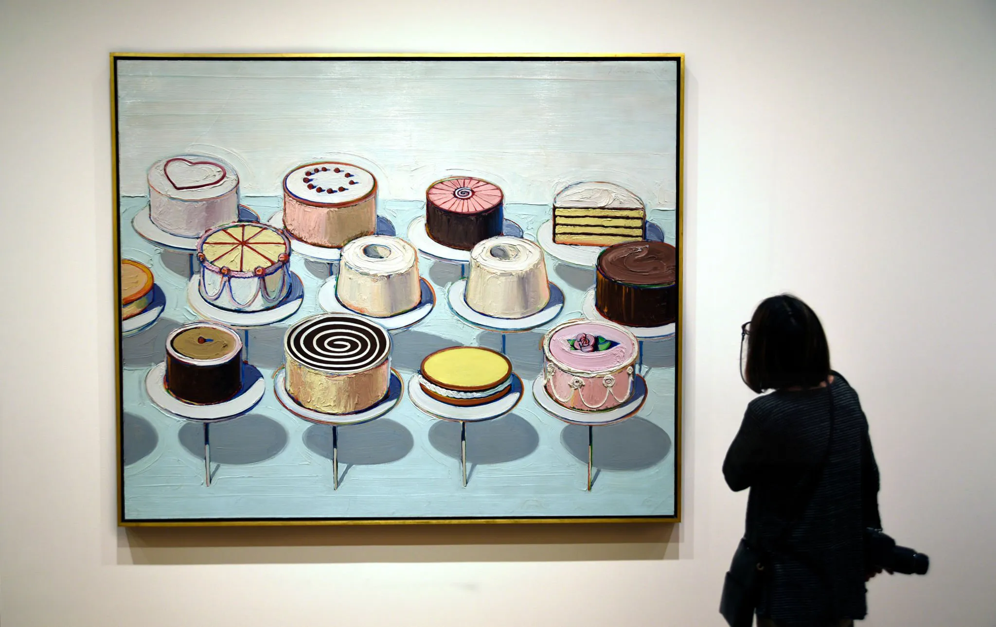 A visitor standing before a large framed painting of cakes on a gallery wall.